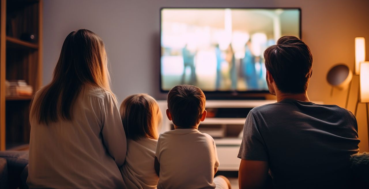 Family watching TV programming from their living room couch, viewed from behind