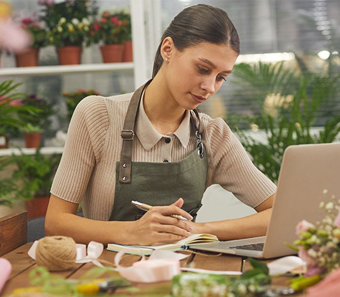 Female small business owner doing work at her laptop in her flower shop