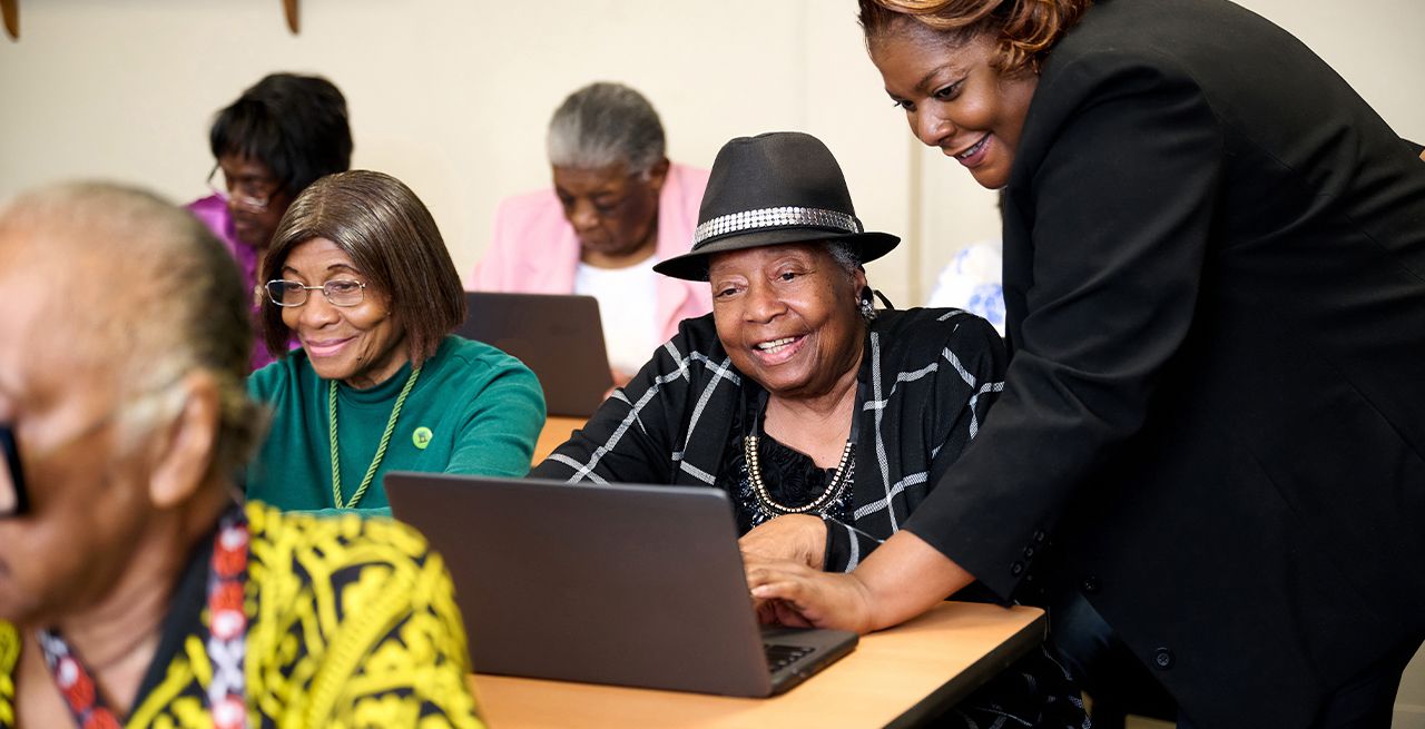 Older woman wearing hat getting instruction on her laptop in a computer lab